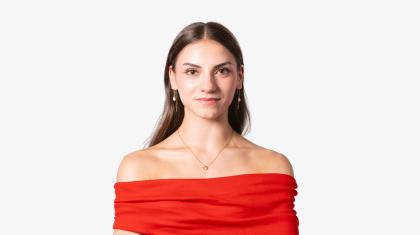 Woman with long, straight, dark hair, wearing a vivid red top, looks directly at the camera