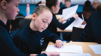 Students in dark tracksuits in a class looking at a worksheet
