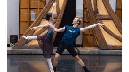 A dancer en pointe arabesque, the other steadying her balance with one hand holding her back and leaning back theatrically